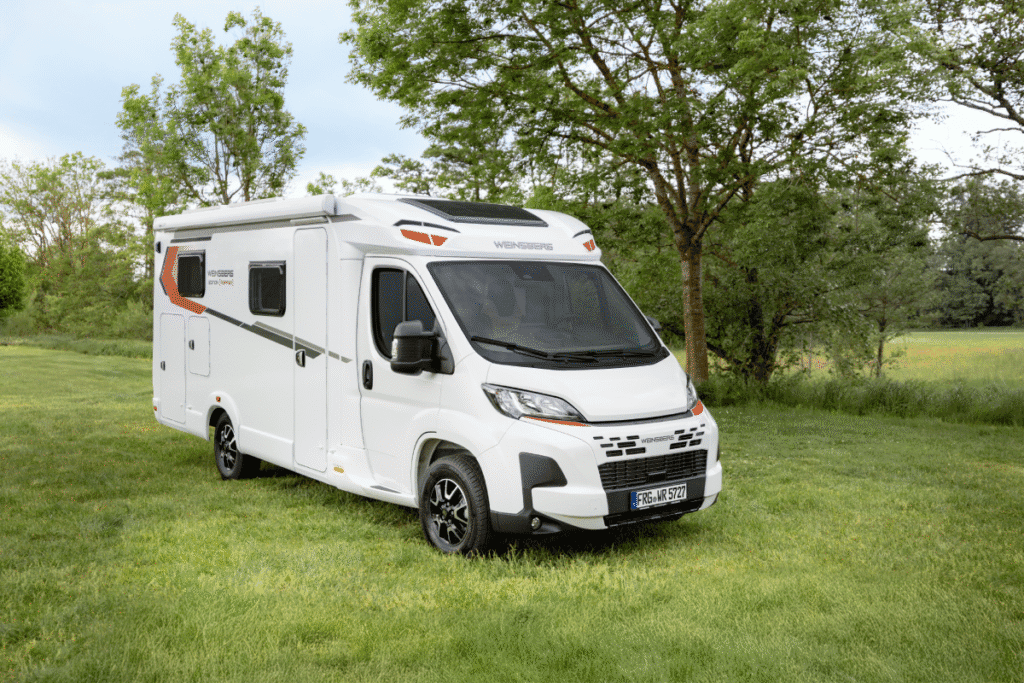 Witte Weinsberg Pepper camper uit 2027, staat in een veld met gras en bomen, omringd door natuur.