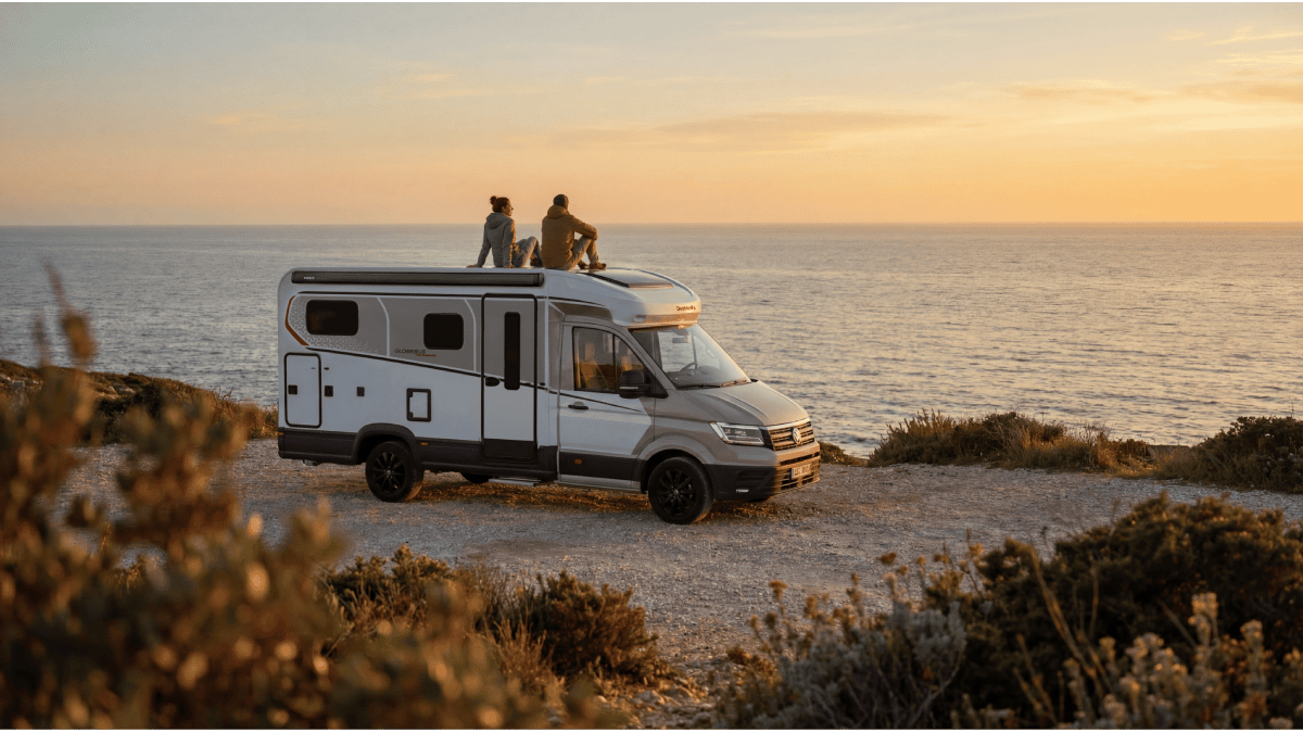 Een stel zit op een campervan met uitzicht op de oceaan, genietend van de zonsondergang.