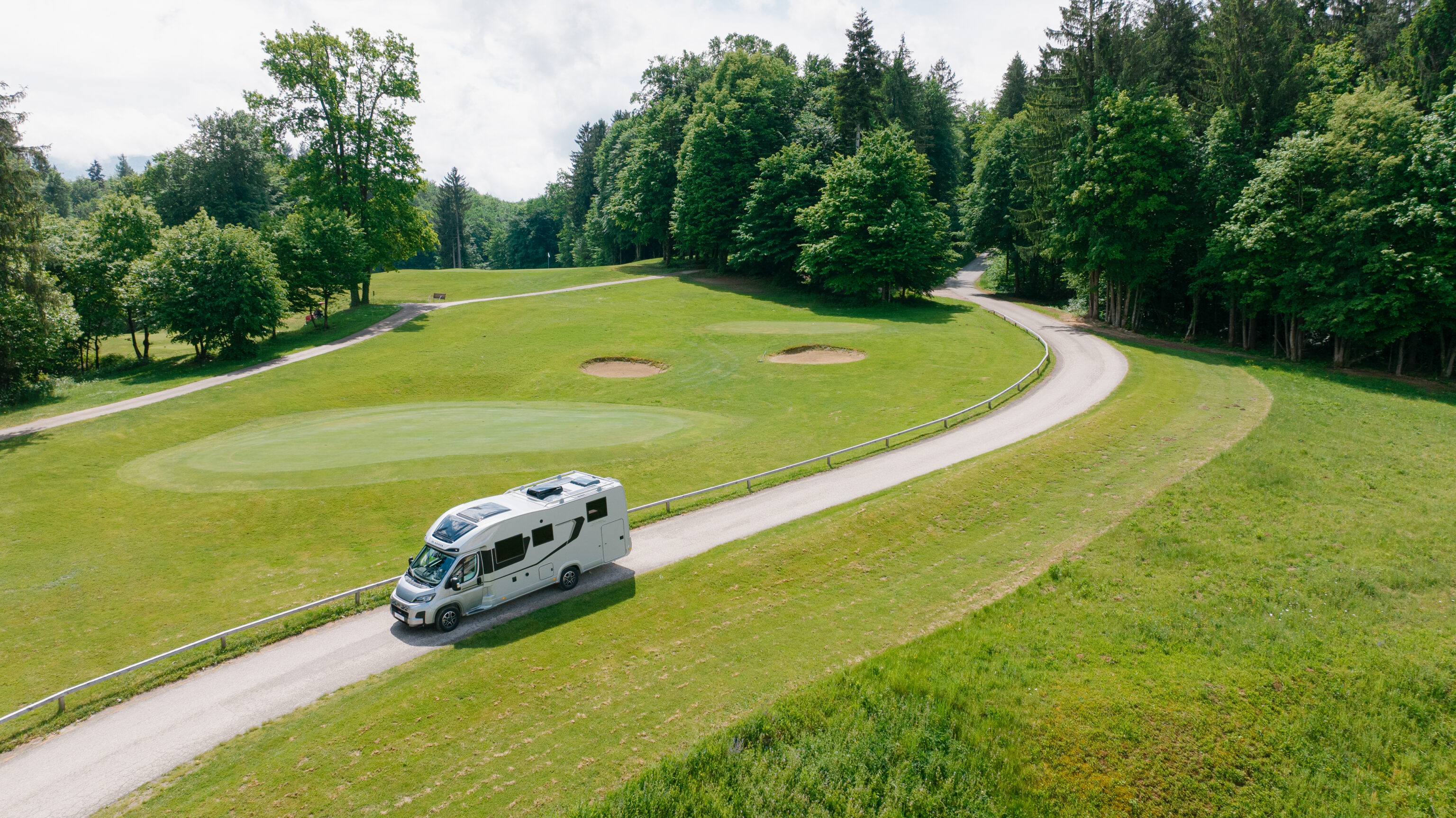 Een Adria Matrix motorhome rijdt door een bosrijke omgeving, met bomen langs de weg.
