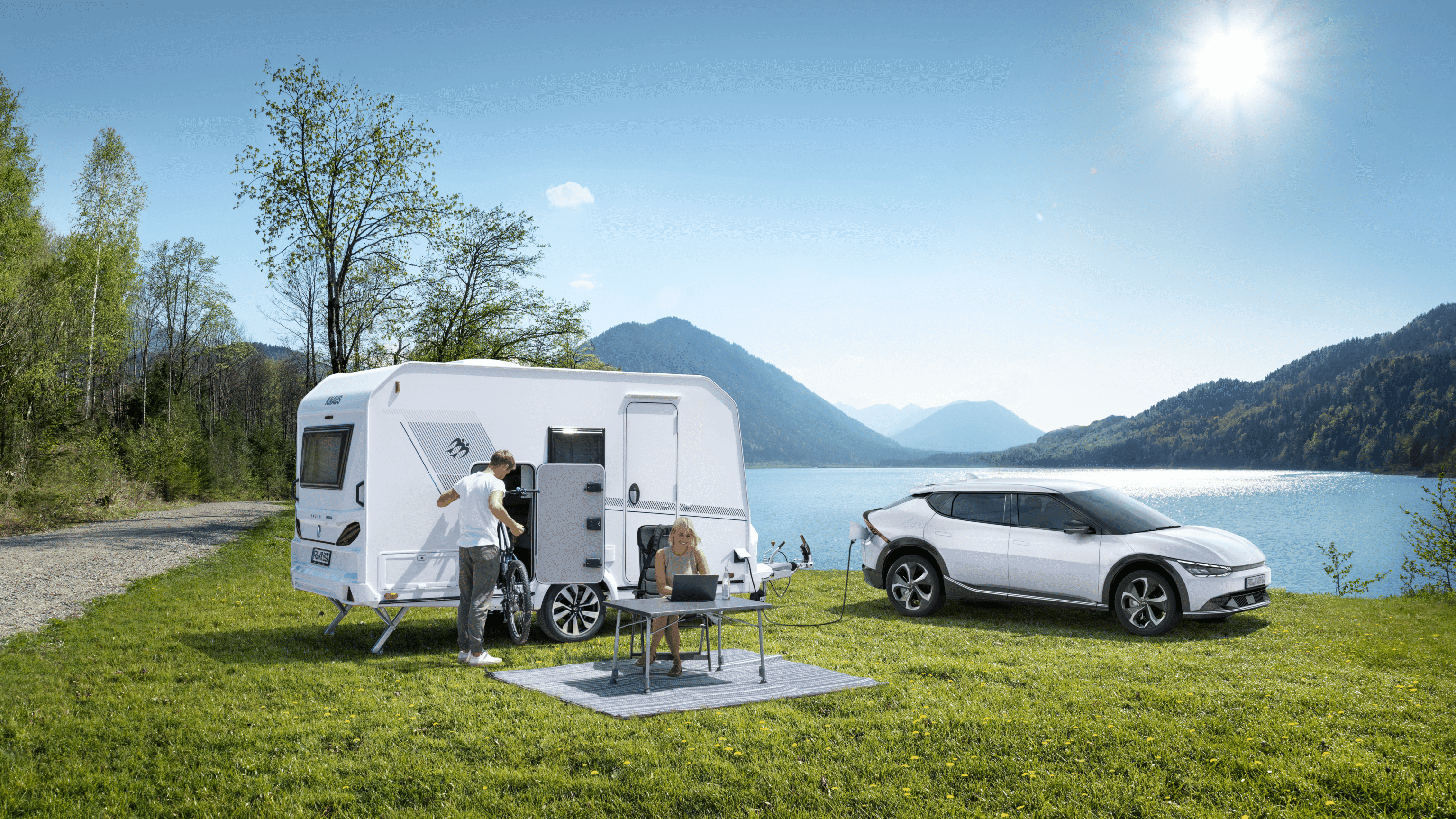 Een kleine, lichtgewichte caravan voor een meer, die aan een elektrische auto staat.